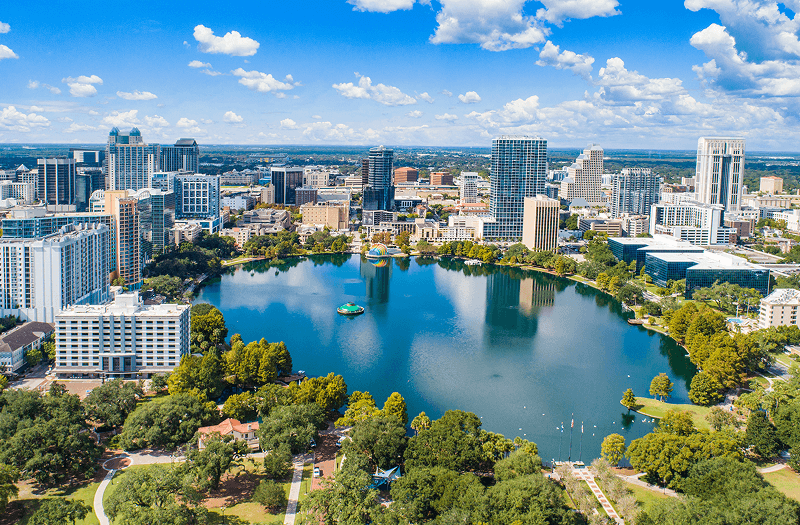 Aerial view of the Orlando skyline with a large round lake surrounded by trees in the foreground.