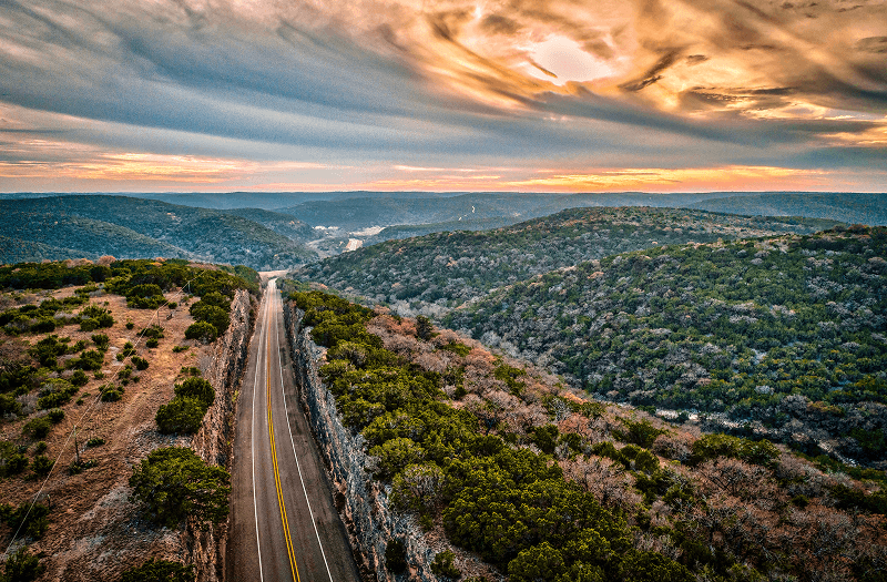 A winding road through Texas Hill Country bathed in warm hues of sunset.