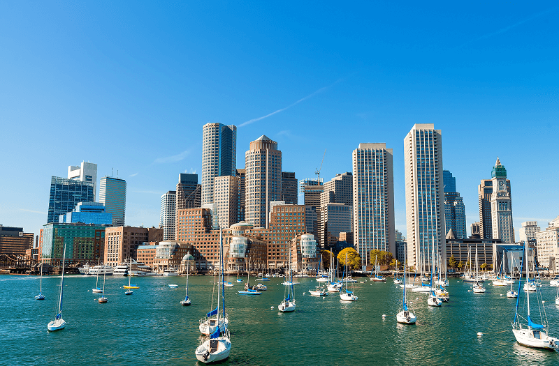  A scenic view of Boston Harbor dotted with boats, with the city skyline visible in the background.