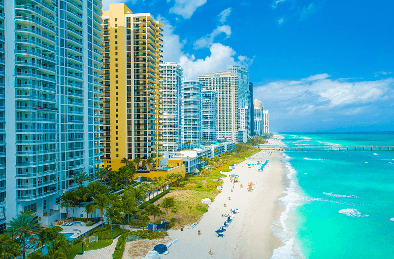 A scenic view of Miami Beach featuring sandy shores, azure waters, and high-rise buildings lining the coast.