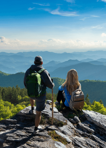 A couple of hikers resting on a large rock and enjoying the scenic mountain views in the distance.