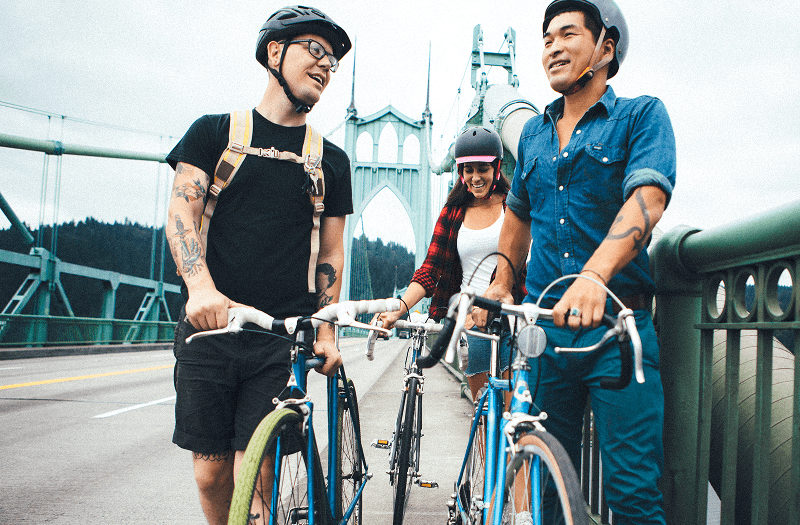 Three people pushing their bikes across a bridge in Portland while chatting and looking at the views.