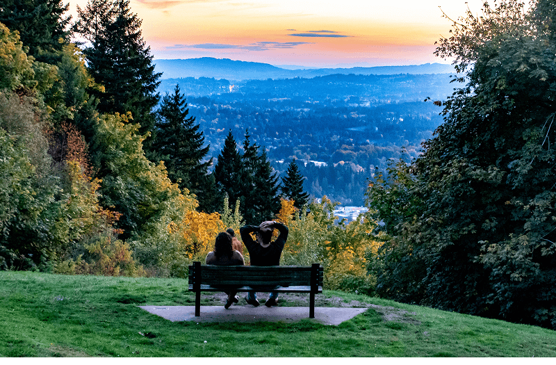 A couple sitting on a bench and enjoying a scenic view of the Portland skyline in the distance.