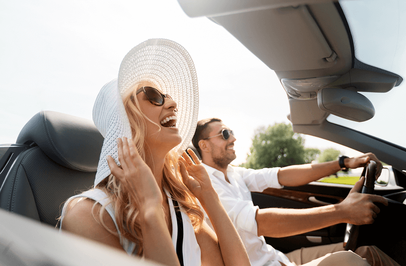  A couple enjoying a sunny day while driving in a convertible car with the top down.