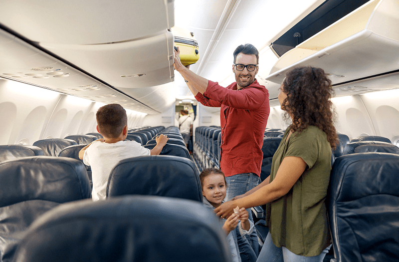 A mom, dad, and two kids grabbing a carry-on as they get ready to exit a plane.