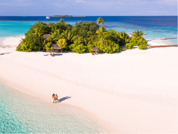 Two people standing on a secluded tropical island in the Maldives, with powdery sand and crystal-clear ocean water.