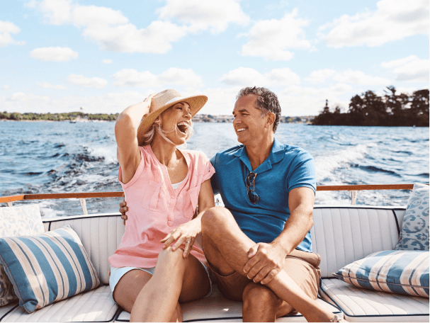A smiling man and woman sitting on the back of a boat as it cruises along open ocean water.