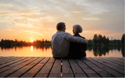 A couple sitting on the edge of a dock, overlooking calm waters at sunset.