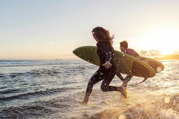 Two people running into the sea with surfboards