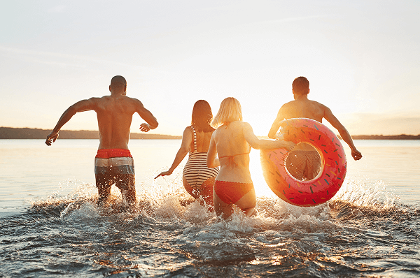 A group of four runs playfully in the water, with one person carrying a bright life ring.