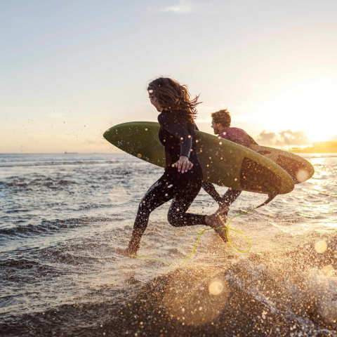 Two people running into the sea with surfboards