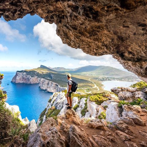 A man enjoying the view of the rocks and the clear blue waters mid-hike.
