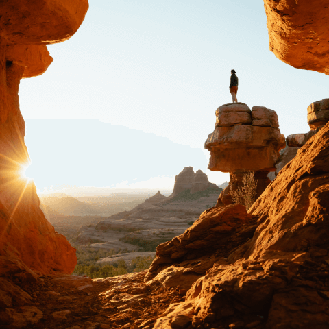 A person standing above a rock, admiring the sunset.