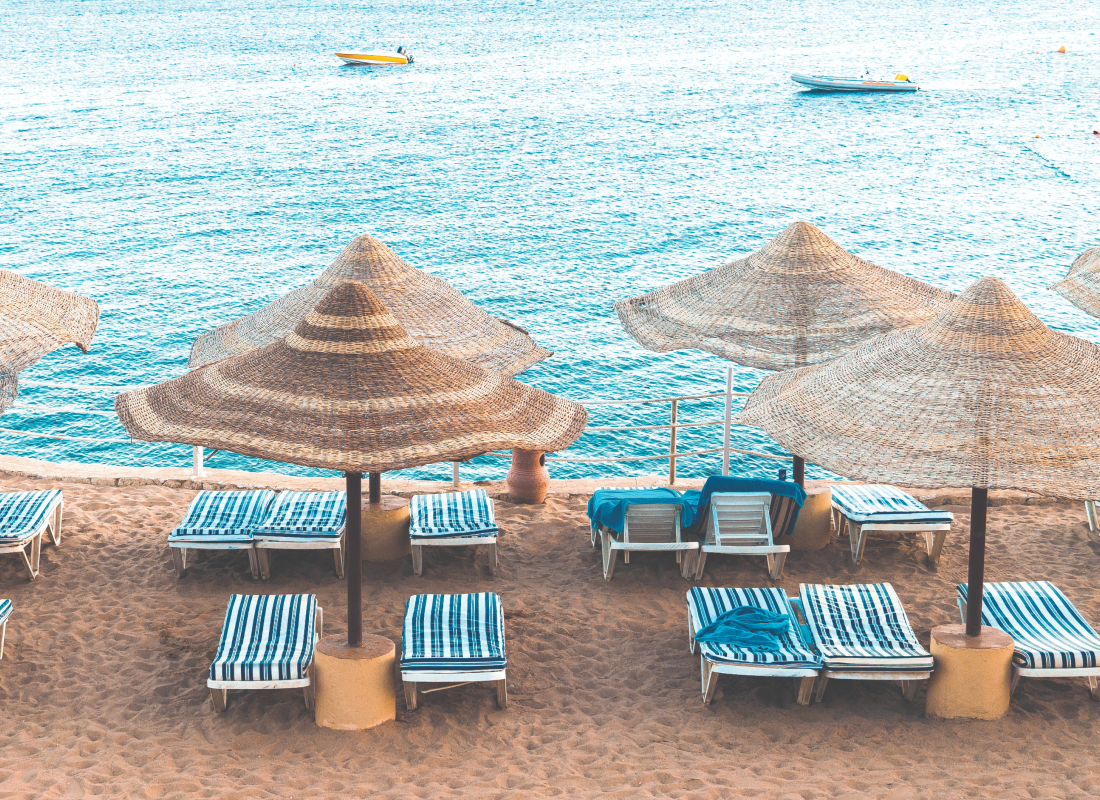 Blue striped lounge chairs with wispy umbrellas next to beautiful waters with a few boats sailing in the distance.