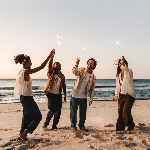 A group of friends merrily playing with sparklers at the beach.