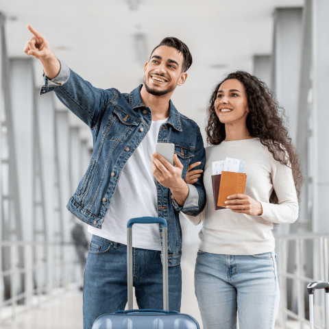 A smiling man pointing ahead while a woman holds their passports and boarding passes.