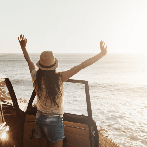 A woman basking in the sunlight and ocean with her hands above her head.