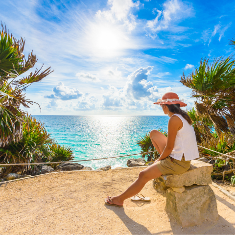 A woman relaxes on a rock, enjoying the view of the ocean and the horizon on a sunny day.