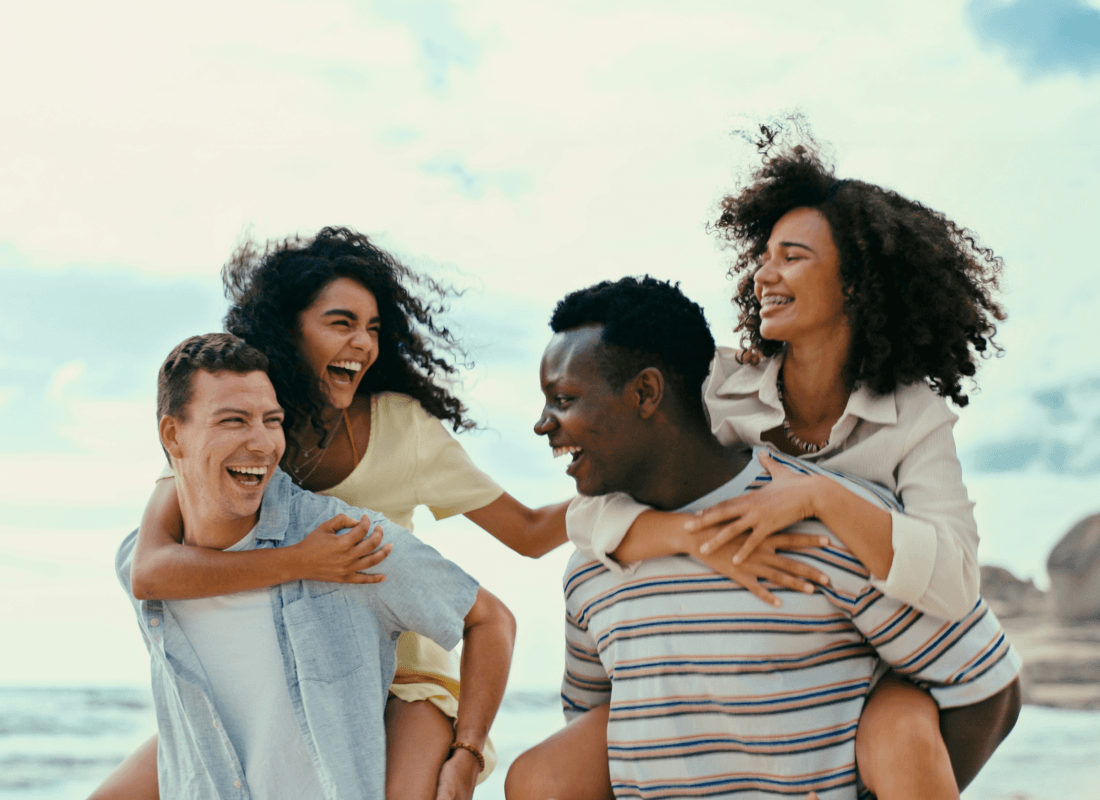 Two young couples giving piggyback rides on a sunny beach.