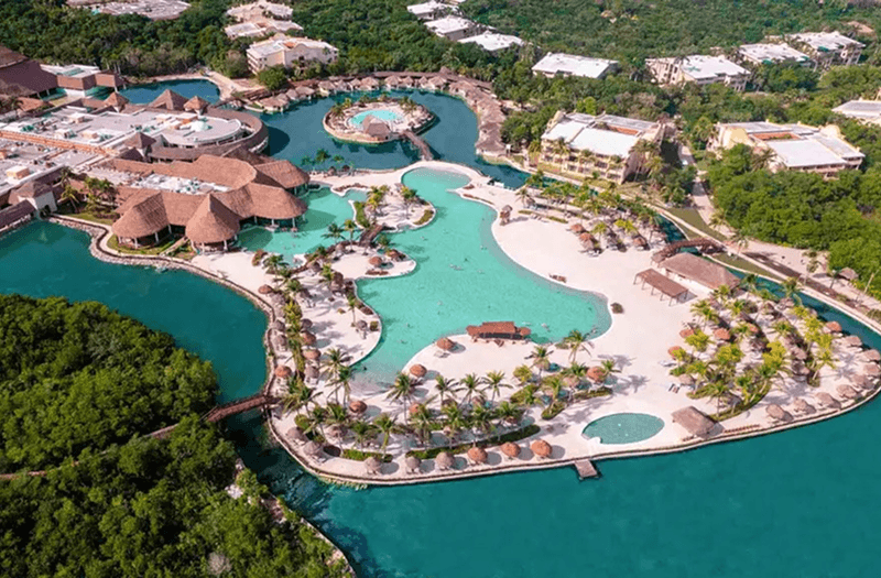 Aerial view of the expansive Grand Palladium Select White Sand in Mexico with a pool, palm trees, and buildings surrounded by a lagoon.