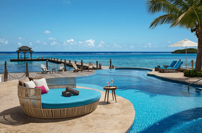 A large lounge chair next to a clear infinity pool overlooking turquoise waters on a bright day at Zoëtry Montego Bay Jamaica.