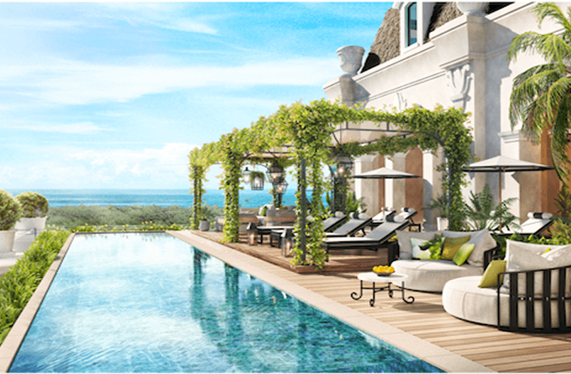 Several lounge chairs on a wooden deck next to a beautiful infinity pool, all overlooking the ocean on a bright afternoon.