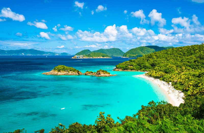 View of island with vegetation near the shore of the beach that has vegetation with more islands and clear sky in the background