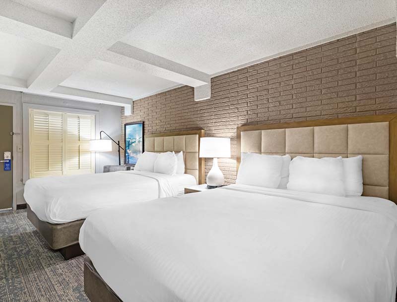 A cozy hotel room in neutral tones, featuring two large beds and modern lighting. 