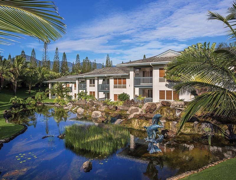 A resort nestled among lush tropical vegetation with a large water feature in front of the building.