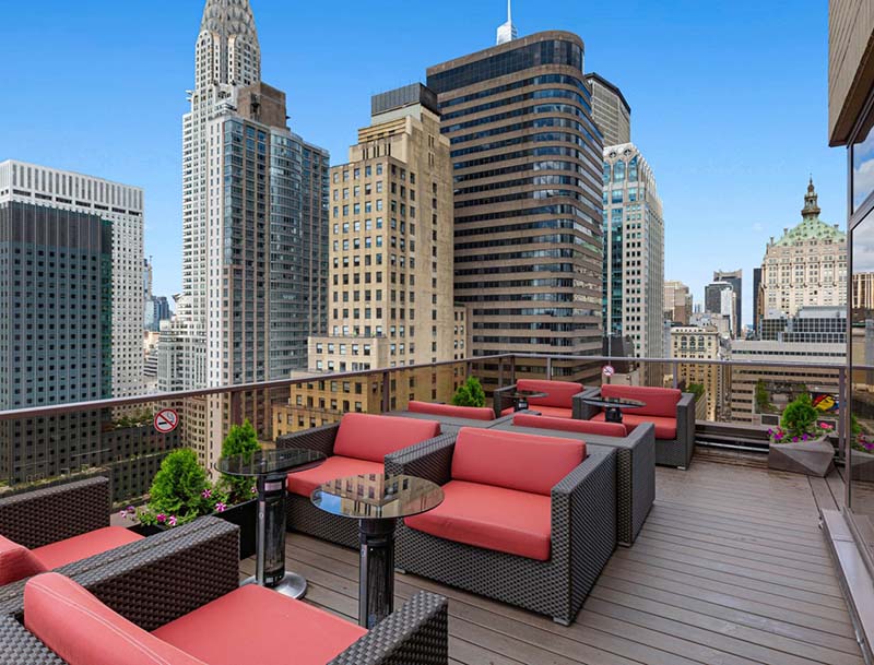 Rooftop patio featuring red couches and tables, offering a scenic view of the city skyline.