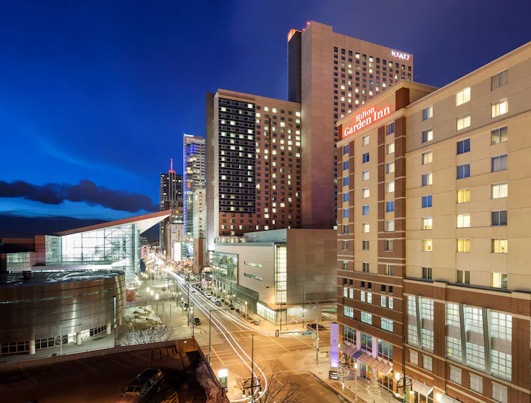 The hotel’s tall brick facade at dusk, overlooking the modern Colorado Convention Center across the brightly lit city street below.
