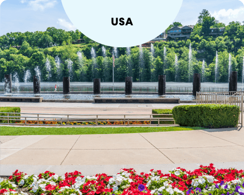 Branson Landing's fountain show on Lake Taneycomo, with water jets, landscaped gardens, and houses nestled atop the lush green hillside.