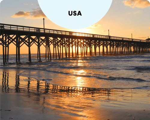 The wooden pier at Myrtle Beach, South Carolina, silhouetted against a golden sunset reflecting on the ocean and wet sand.