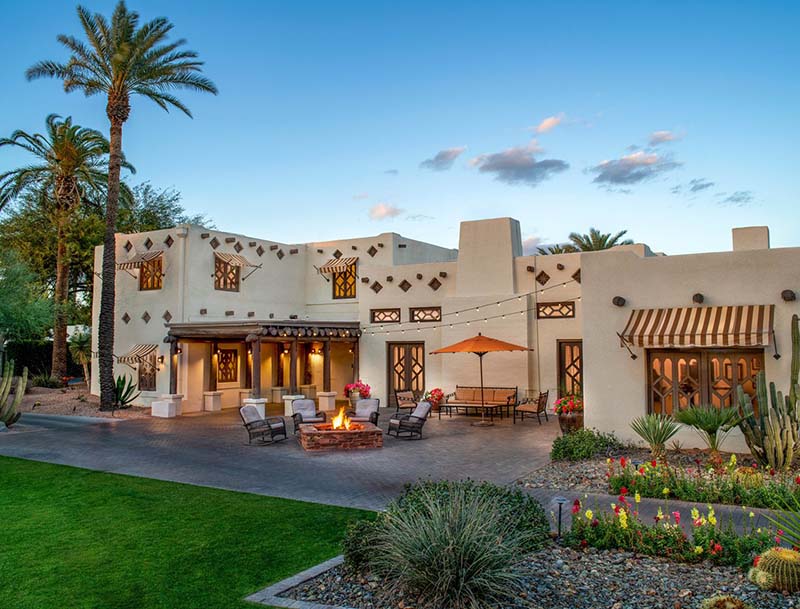 An adobe-style building with a seating area and a burning firepit in the front.