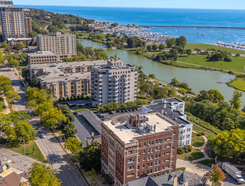 An elevated city view in Wisconsin showing high-rise residential buildings and tree-lined streets next to a marina packed with boats on a vast blue lake.