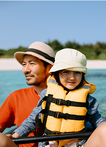 An adult and a child wearing a life jacket with out of focus beach in the background