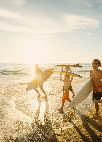 A group of people and children cheerfully running towards the ocean with surfboards in hand.