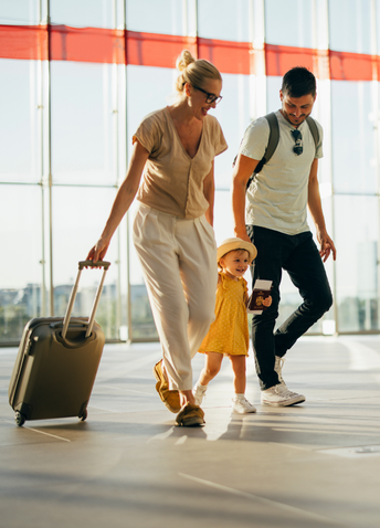 A young couple and their child walking together through an airport terminal, carrying luggage and travel documents.