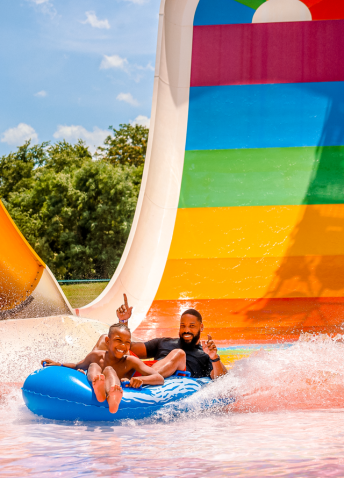 A man and a child riding an inflatable tube down a colorful water park ride.