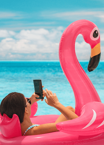 A woman using her mobile device while floating on an inflatable pink flamingo tube.