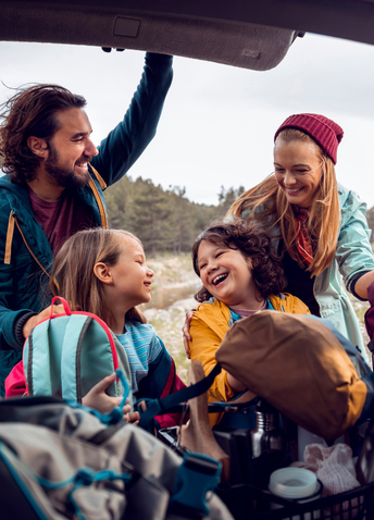 A happy family unloading backpacks from the trunk of their car during an outdoor autumn road trip.