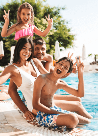 A happy family of four posing together by a resort swimming pool while making peace signs.