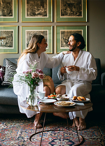 A couple in robes enjoying a light meal on a couch