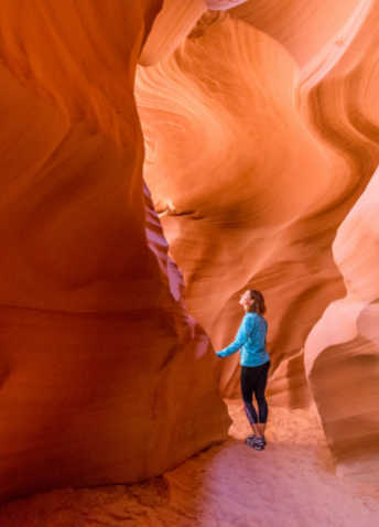 A woman walking in a sunlit red rock cave formation