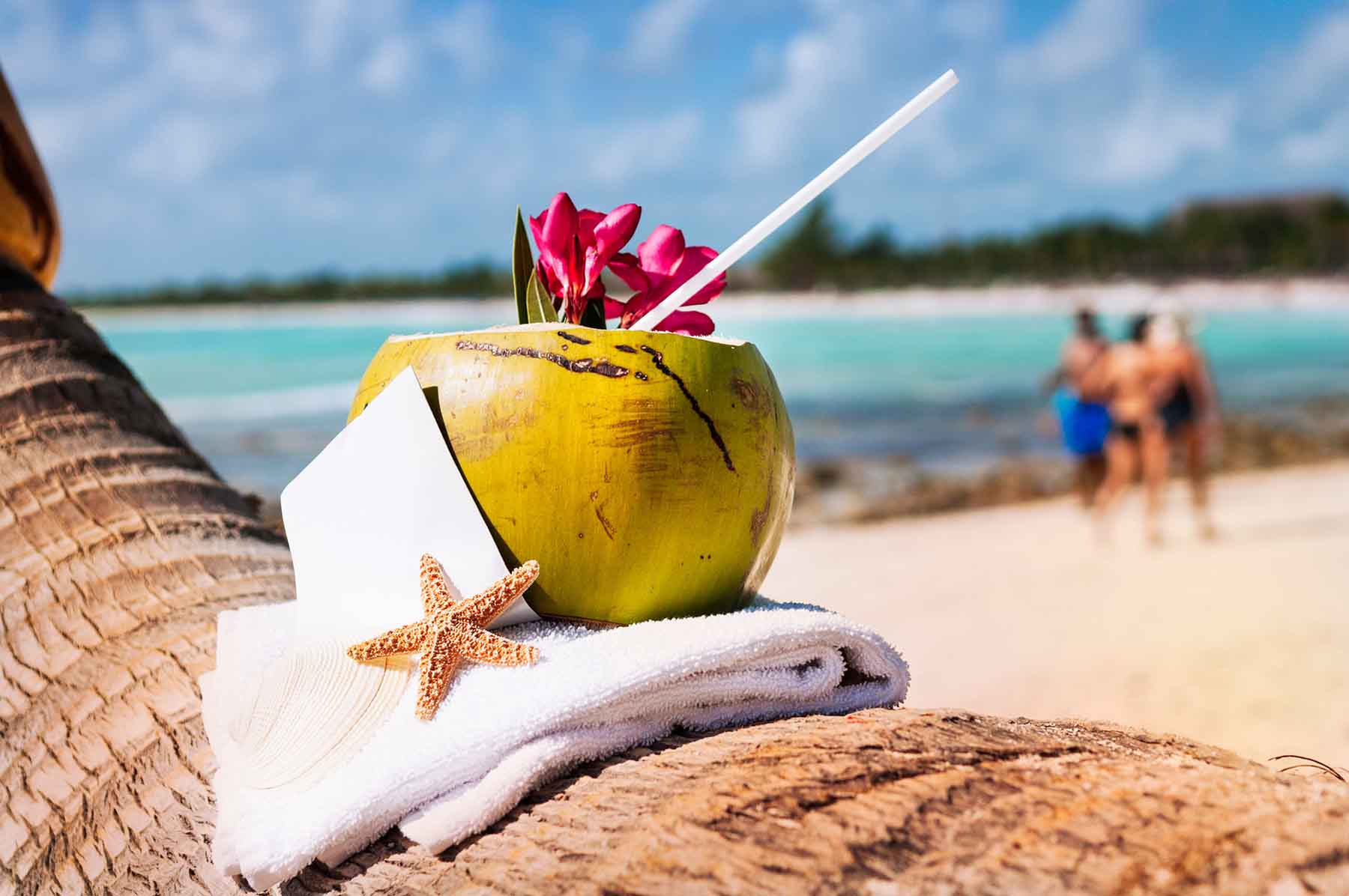 An adorned coconut drink rested on a palm tree of Cancun with people walking in the background.
